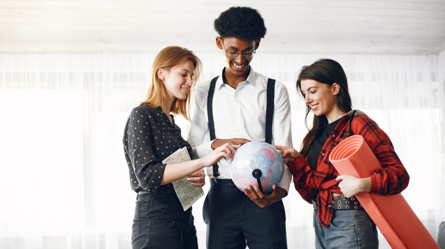 Diverse friends are going for a journey. They are planning using the globe. Bright living room.